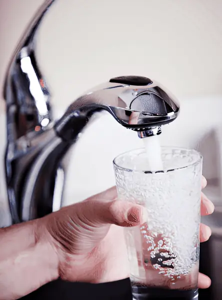 A person filling a glass of water from a faucet with a water softener system.