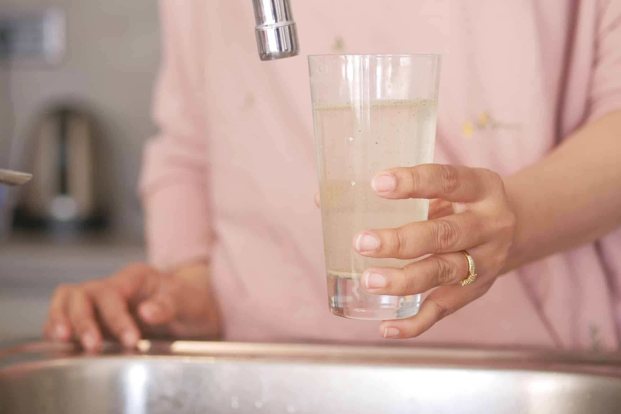 dirty water pouring from a faucet tap in a glass,