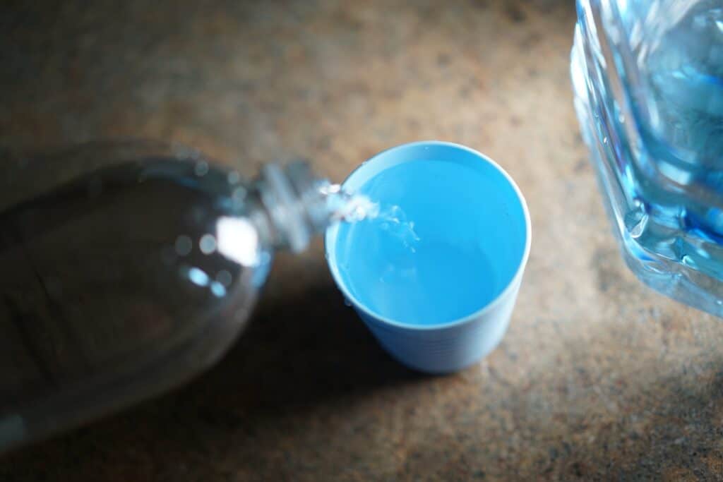 Pouring water into a blue cup to demonstrate the importance of understanding water softener grain capacity for the best water quality.