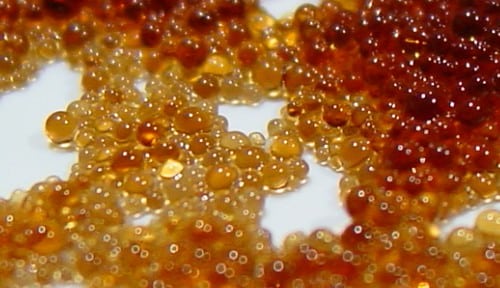 A close-up shot of amber-hued water softener resin beads, an ion-exchange medium designed to reduce mineral content, enhance water quality, and improve overall taste.