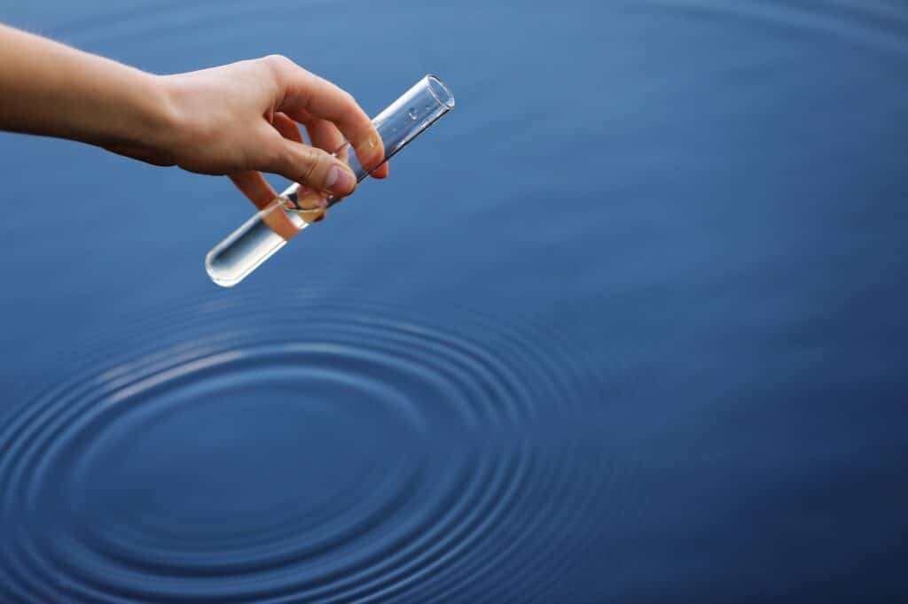 Hand collecting water with a test tube to measure water hardness levels in order to calculate the required water softener grain capacity.